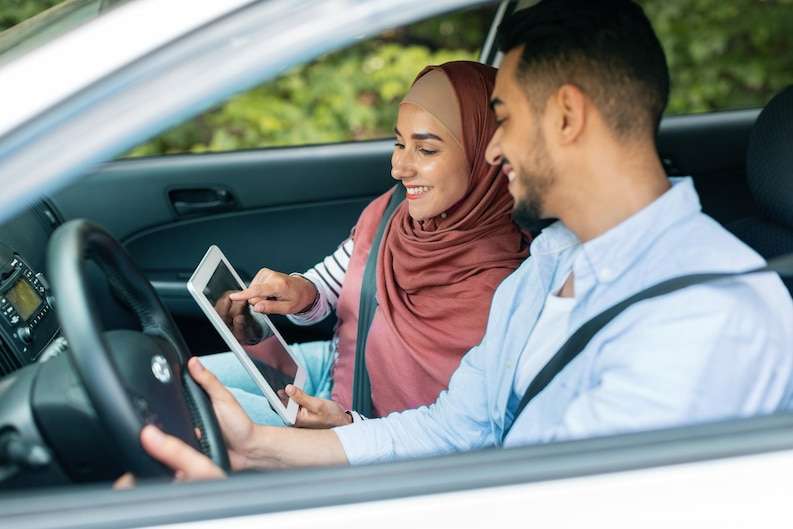 [freepicdownloader com] cheerful millennial muslim female hijab shows way tablet with empty screen husband steering wheel car medium ()Madinah airport to hotel taxi service